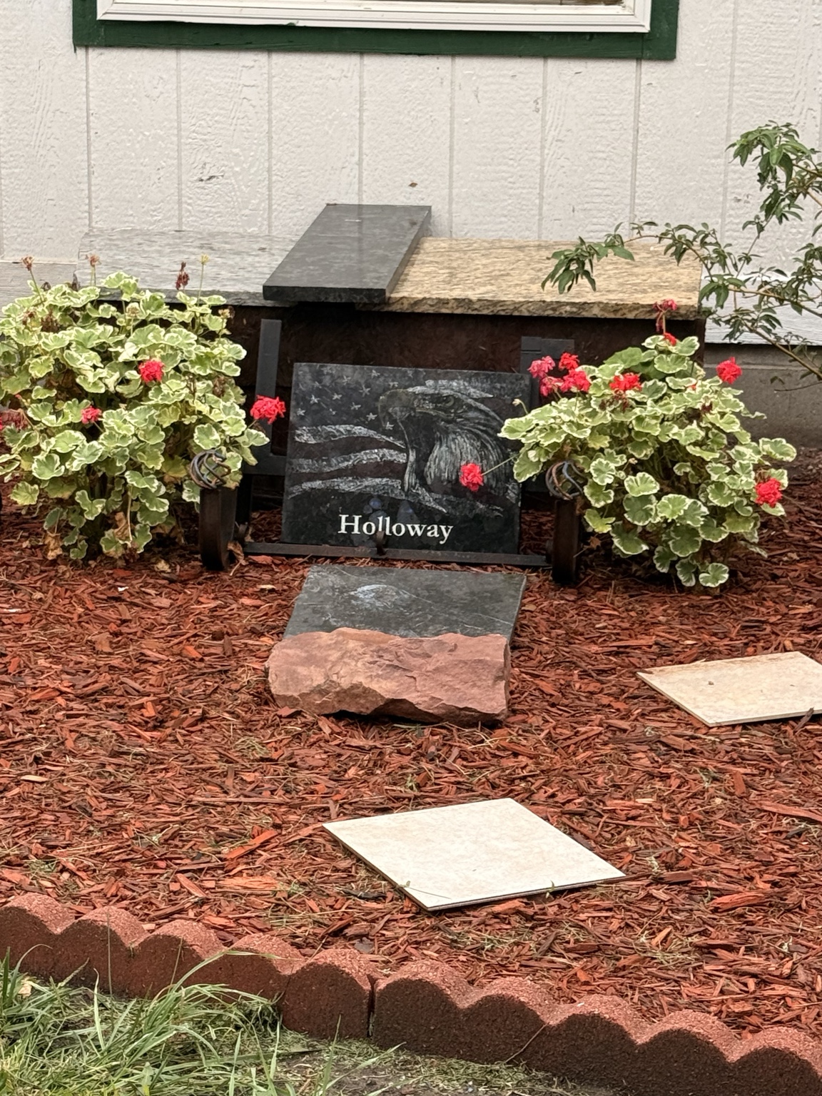 Holloway’s eagle and flag tribute displayed between red flowers in his garden